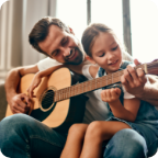 A father teaches his young daughter to play the acoustic guitar. 